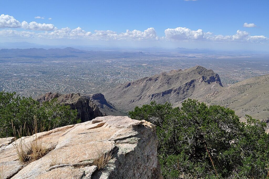 A panoramic view of Northwestern suburbs of Tucson, with urban clusters nestled amidst the vast desert, as seen from the elevated vantage of the Santa Catalina Mountains.