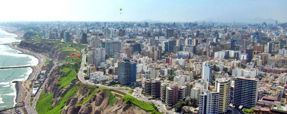 Arial view capturing the sprawling skyline of Miraflores with modern buildings and coastline in the background.