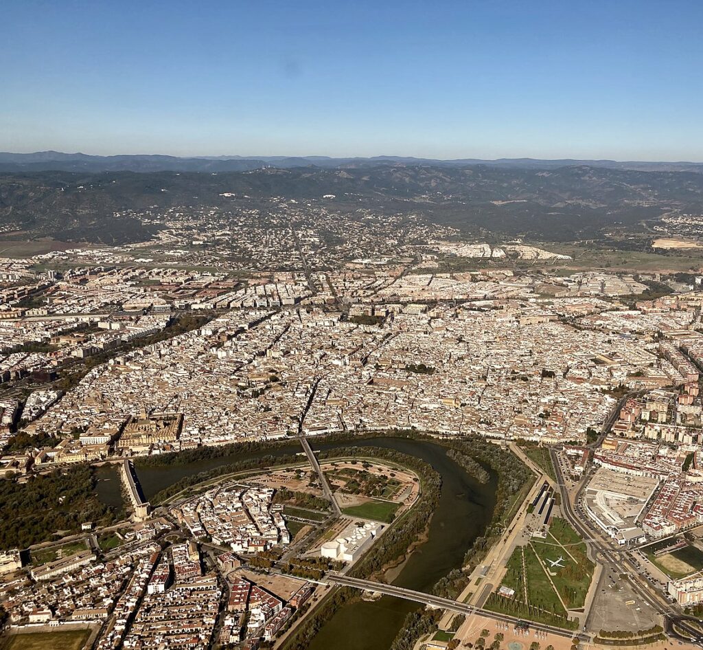 Aerial view of Cordoba, Spain showcasing the city's historic center with the Guadalquivir River winding through, and the distant Sierra Morena mountains.